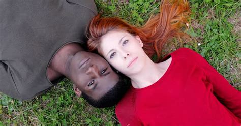 Serious Interracial Young Couple Lying On Lawn Turning Heads In