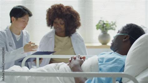 African American Patient Lying With Nasal Cannula On Bed In Hospital Ward And Discussing