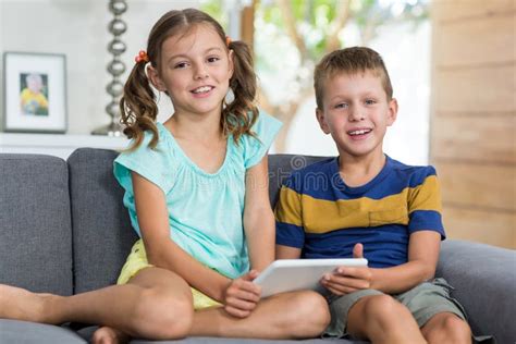 Portrait Of Siblings With Digital Tablet Sitting On Sofa In Living Room Stock Image Image Of