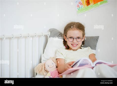 Cute Girlie In Glasses Reading A Book While Lying In Bed Next To Her