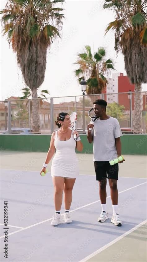 Couple Walking On The Tennis Court And Chatting And Smiling Holding