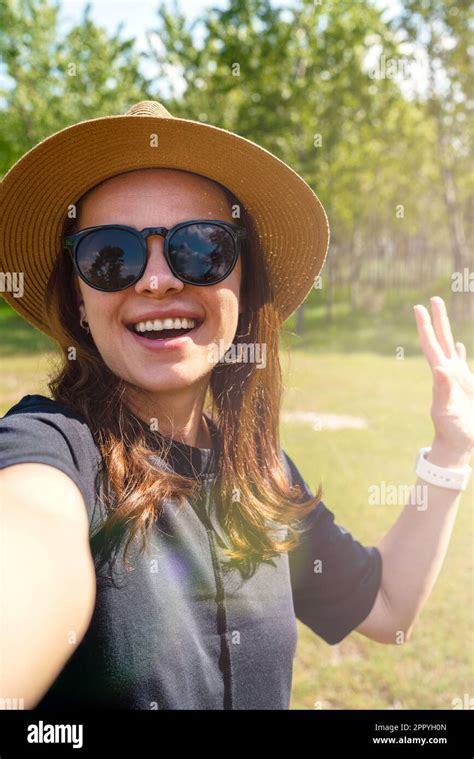 Woman Wearing Sunglasses And Straw Hat Waving Hand And Taking A Selfie