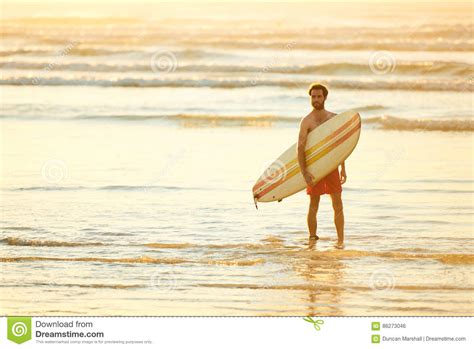 Young Male Surfer At The Beach For Sunrise With Surfboard Stock Photo