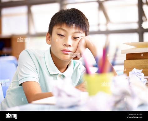 Sad And Frustrated Asian School Boy Sitting Alone In Classroom With
