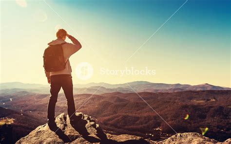 Man Standing At The Edge Of A Cliff Overlooking The Mountains Below