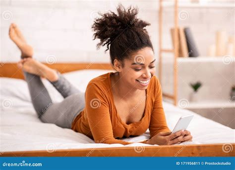 African American Woman Using Smartphone Lying In Bed At Home Stock