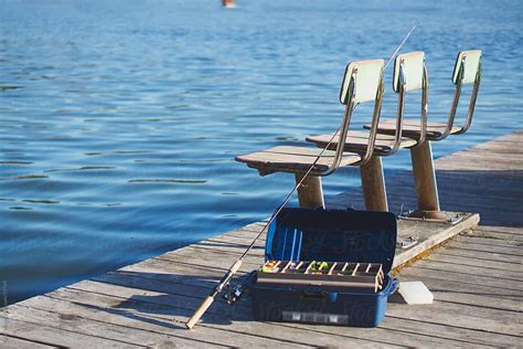 A Fishing Pole And Tackle Box Sit On A Dock Next To Old Fishing Chairs