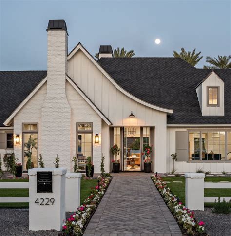 This gorgeous modern farmhouse features hardie board board and batten siding with stunning black framed pella windows. Charm = White farmhouse at night with sweeping roofline ...