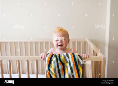 Baby Boy Crying While Standing In Crib Against Wall At Home Stock Photo