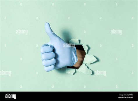Hand In Medical Glove With Thumb Up Gesture Through Hole In Paper Wall