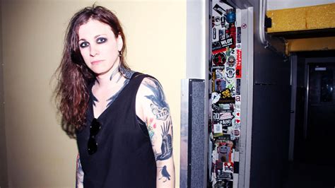 A Woman With Tattoos Standing Next To A Wall