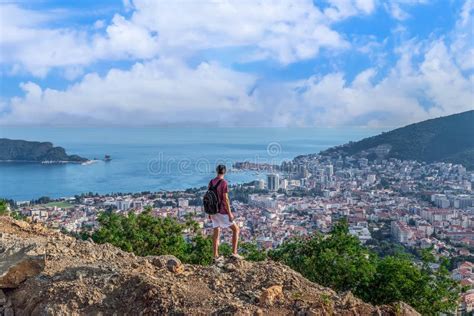 A Male Tourist Stands On Top Of A Mountain And Looks Down At Budva