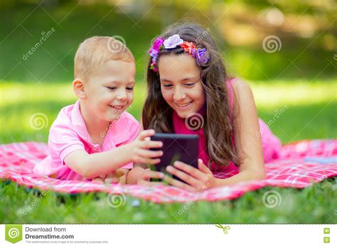 Sister And Brother Lying Down On Blanket And Using Tablet Stock Photo