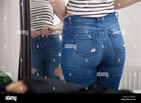 A Woman At Home Pulling On Tight Jeans In Front Of A Bedroom Mirror
