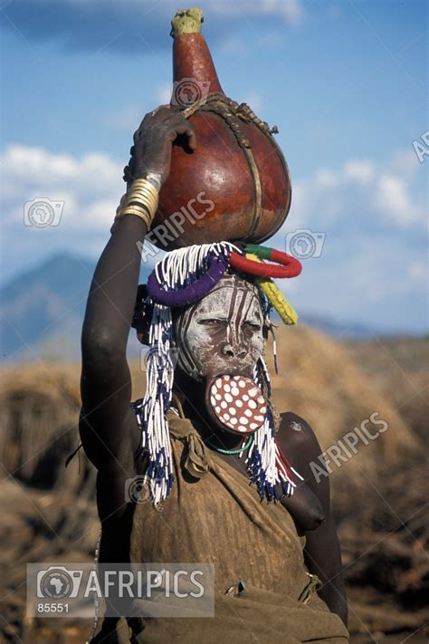 afripics mursi woman with elaborate beaded headdress and lip plate carrying a calabash on her