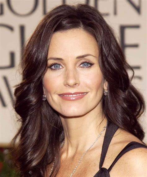 a woman with long brown hair and blue eyes smiles at the camera while wearing a black dress