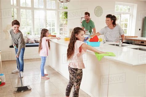 Children Helping Parents With Household Chores In Kitchen Stock Photo
