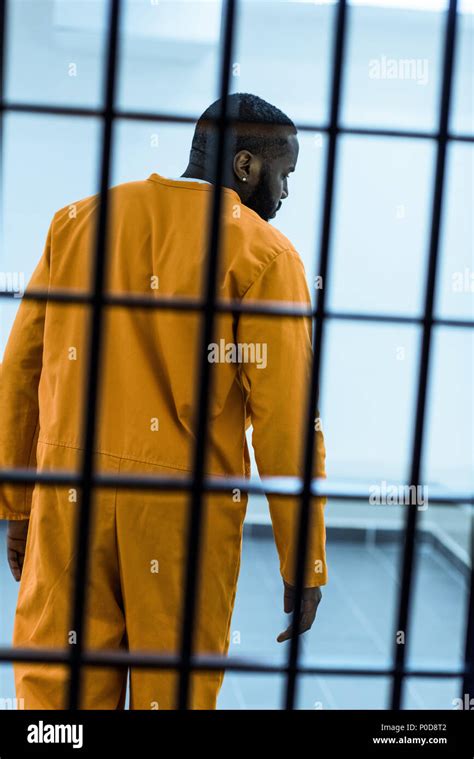 Rear View Of African American Prisoner Behind Prison Bars Stock Photo