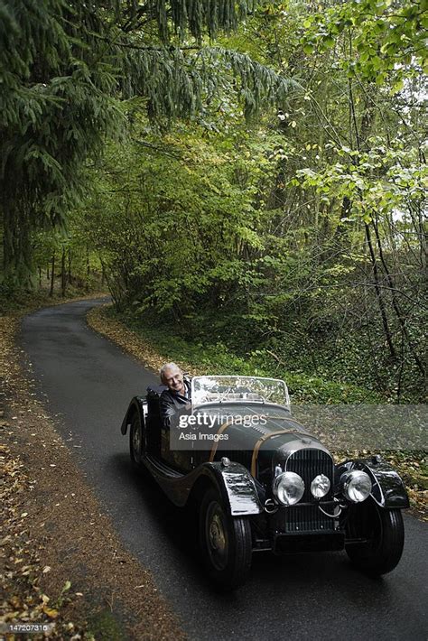 Senior Man Driving Down Country Road In Antique Car High Res Stock
