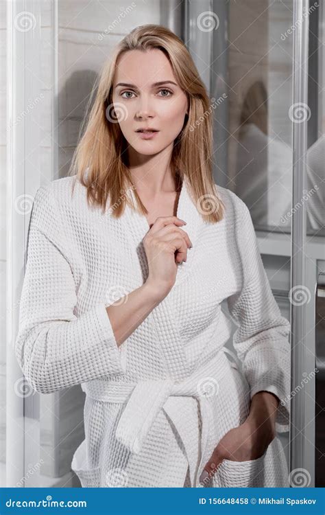 Attractive Middle Age Blond Woman In White Bathrobe In Bathroom He Enters The Glass Shower And