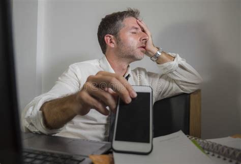 Upset And Stressed Businessman Holding Phone Working At Computer Desk