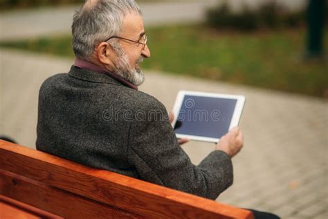 Grandpa Use A Tablet Sitting In The Park On The Bench Stock Photo