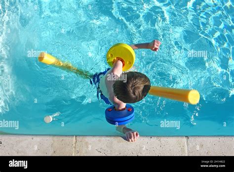 Top View Of Little Boy Floating In Swimming Pool With Floats And Arm