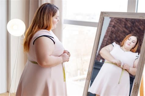 Mulher gordinha e simpática olhando no espelho enquanto mede a cintura Foto Premium