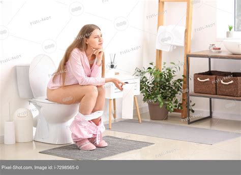 Молодая женщина сидит на унитазе в туалете Стоковая фотография