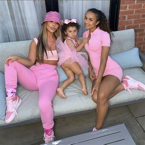 Three Women In Pink Outfits Sitting On A Couch With One Holding A Baby