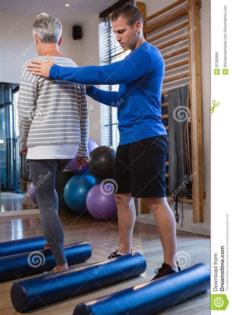 Physiotherapist Assisting Senior Woman In Performing Exercise On Foam