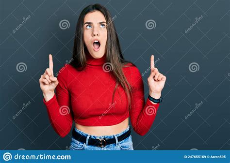 Young Brunette Teenager Wearing Red Turtleneck Sweater Amazed And Surprised Looking Up And