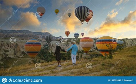 Happy Young Couple During Sunrise Watching The Hot Air Balloons Of