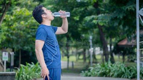 A Stylish Young Asian Man Drinking Water From A Plastic Bottle After