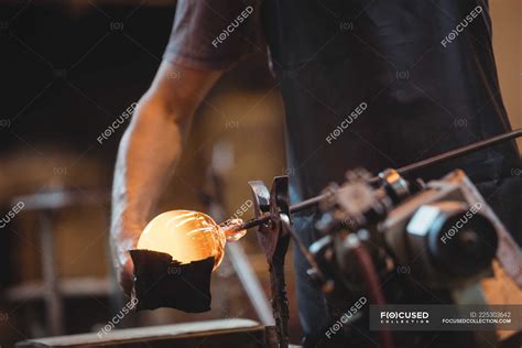 Mid Section Of Glassblower Forming And Shaping A Molten Glass At Glassblowing Factory