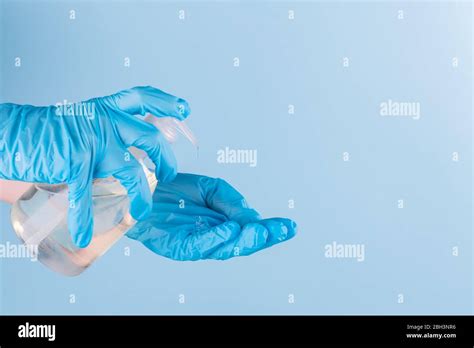 Female Hand In Latex Surgical Gloves Is Using Antiseptic Hand Sanitizer Blue Background