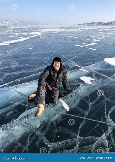 Tourist Sitting On The Surface Of The Cracks Of The Frozen Lake Baikal