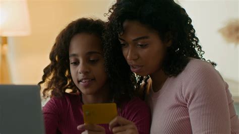 Young African American Mother Teaching Her Daughter To Shop Online
