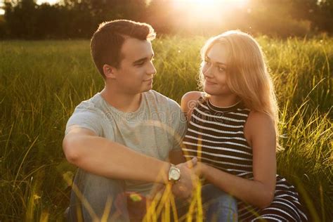 Young Happy Couple Sitting Together On Grass Holding Their Hands Stock