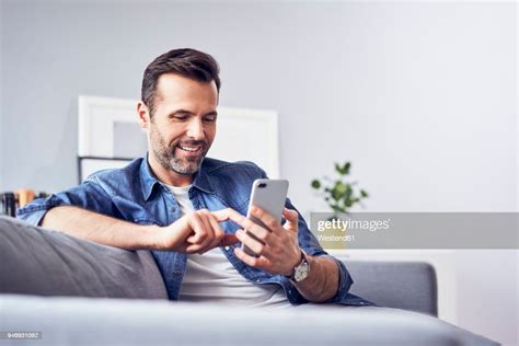 Smiling Man Sitting On Sofa Using Cell Phone Photo Getty Images