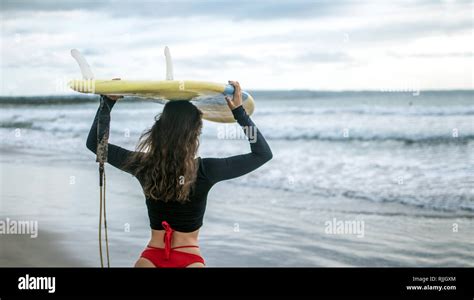 Beautiful Surfer Girl Walking Down To The Beach For Sunset Surf Session Carrying Surfboard On