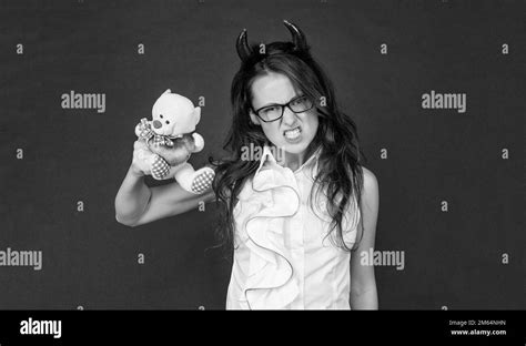 angry girl with red devil horns make scary face holding valentines bear dark background