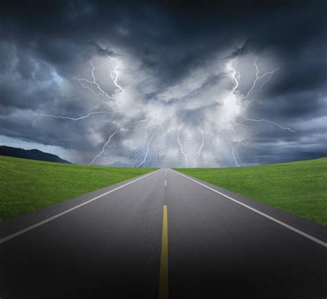 Rainstorm Clouds And Lightning With Asphalt Road And Grass Stock Photo
