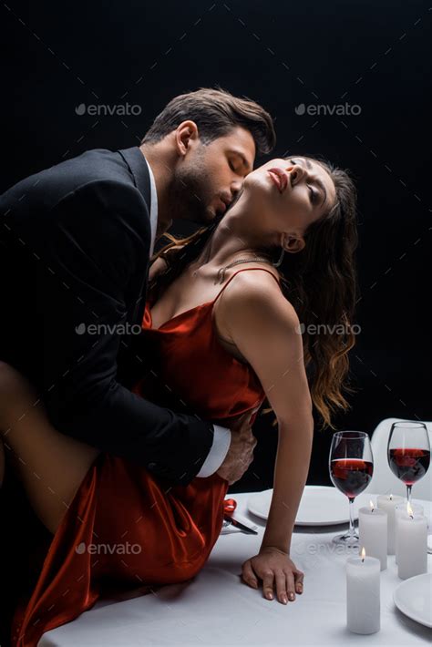 Side View Of Handsome Man Kissing Beautiful Woman In Neck On Served Table Isolated On Black