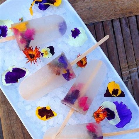 Four Popsicles With Edible Flowers On Them Sitting On Top Of Ice In A Tray