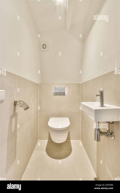 Interior Of Narrow Restroom With Sink And Wall Hung Toilet With White