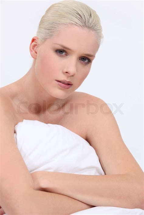 blonde frau nackt sitzt auf dem bett mit einem neutralen gesichtsausdruck stock bild colourbox