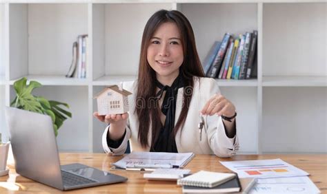 Miniature House In The Hands Of An Asian Woman Real Estate Agent Home Loan Working At The Office