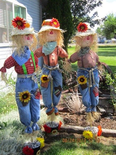 Three Scarecrows With Hats And Sunflowers On Their Heads Are Standing In Front Of A House