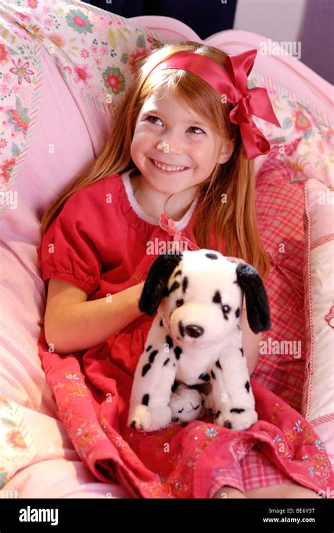 Little Girl Wearing A Romantic Red Dress Sitting On Her Bed And Playing